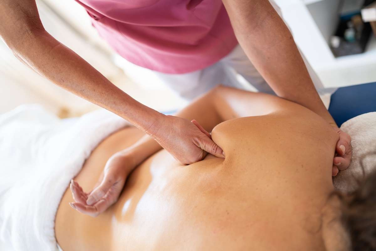 Crop female osteopathic therapist massaging back of patient