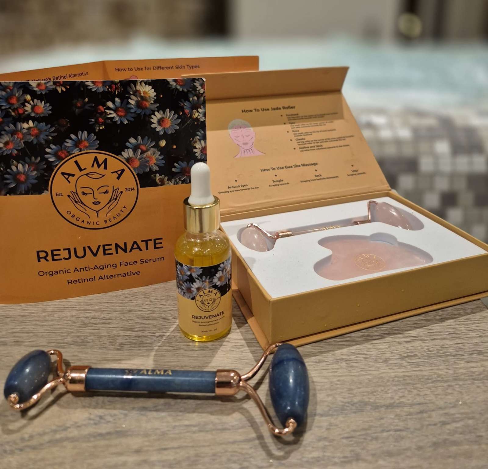 Alma's Rejuvenate anti-aging face serum placed on a soft surface alongside a rose quartz gua sha tool and branded pouch, highlighting natural skincare elegance