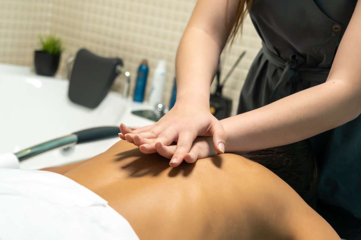 Close-up of a massage therapist pressing firmly on a client’s back with both hands in a modern spa setting.